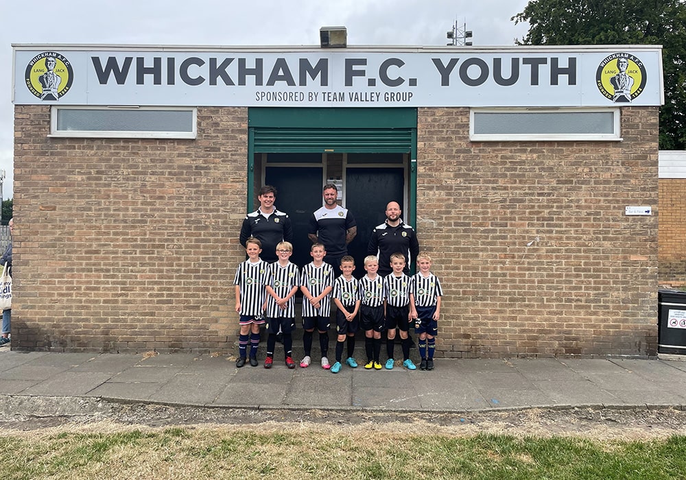 Whickham FC Youth group posed in front of new Team Valley Group sponsor signage.  