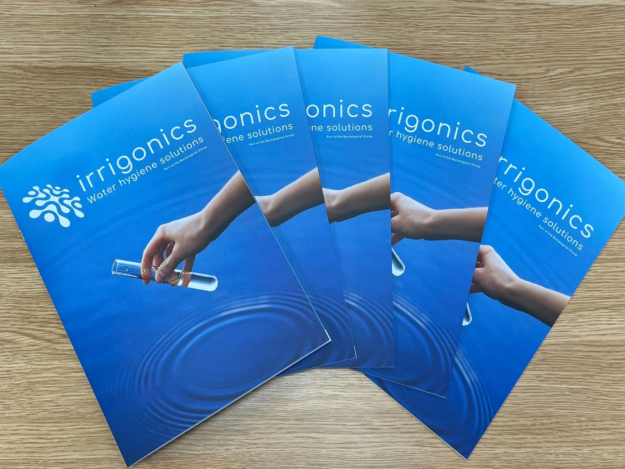 Five business brochures for Irrigonics fanned out on a wooden table. 